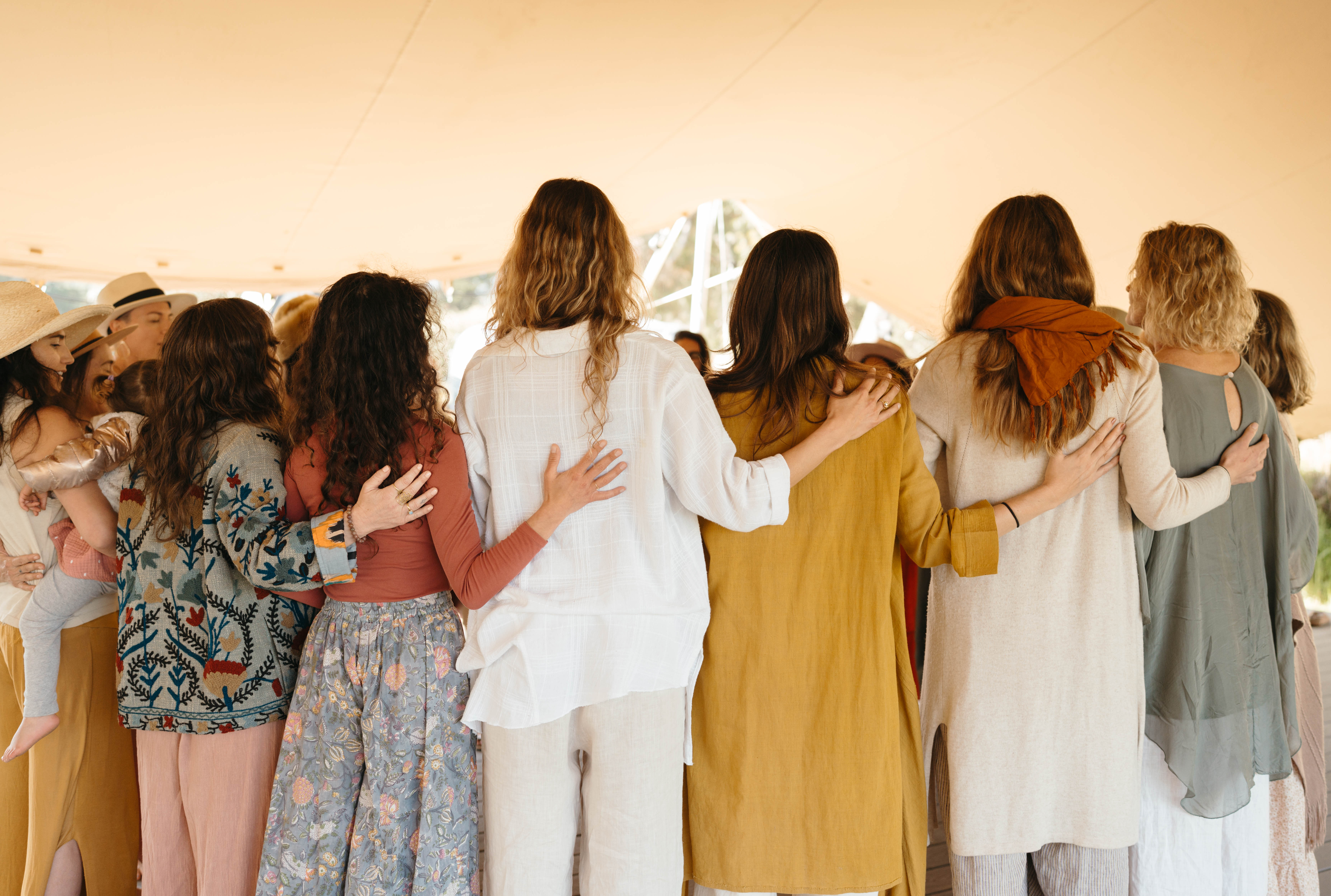 A circle of women standing arm in arm, seen from behind