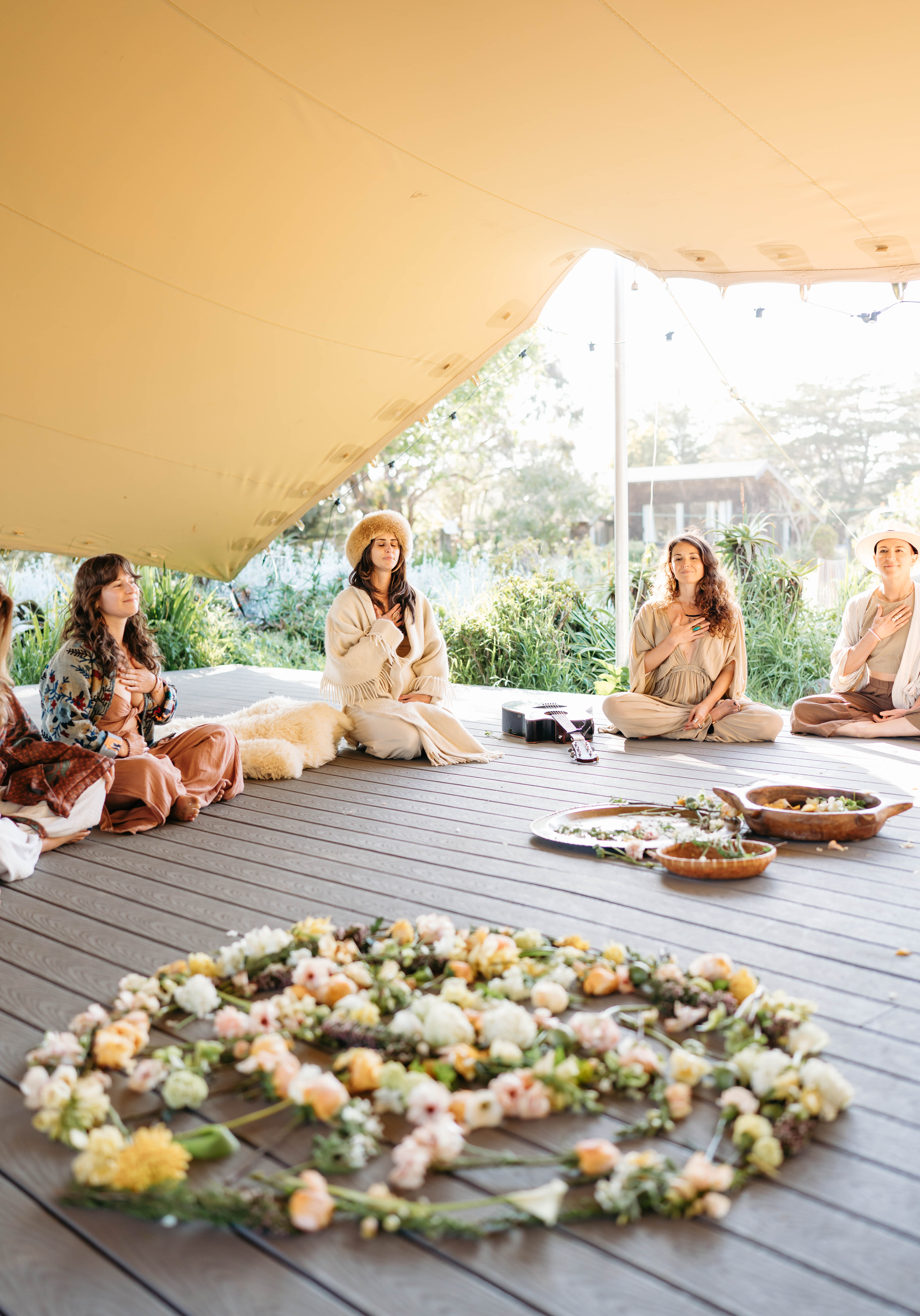 Women sitting in a circle under a canopy around a mandala of flowers